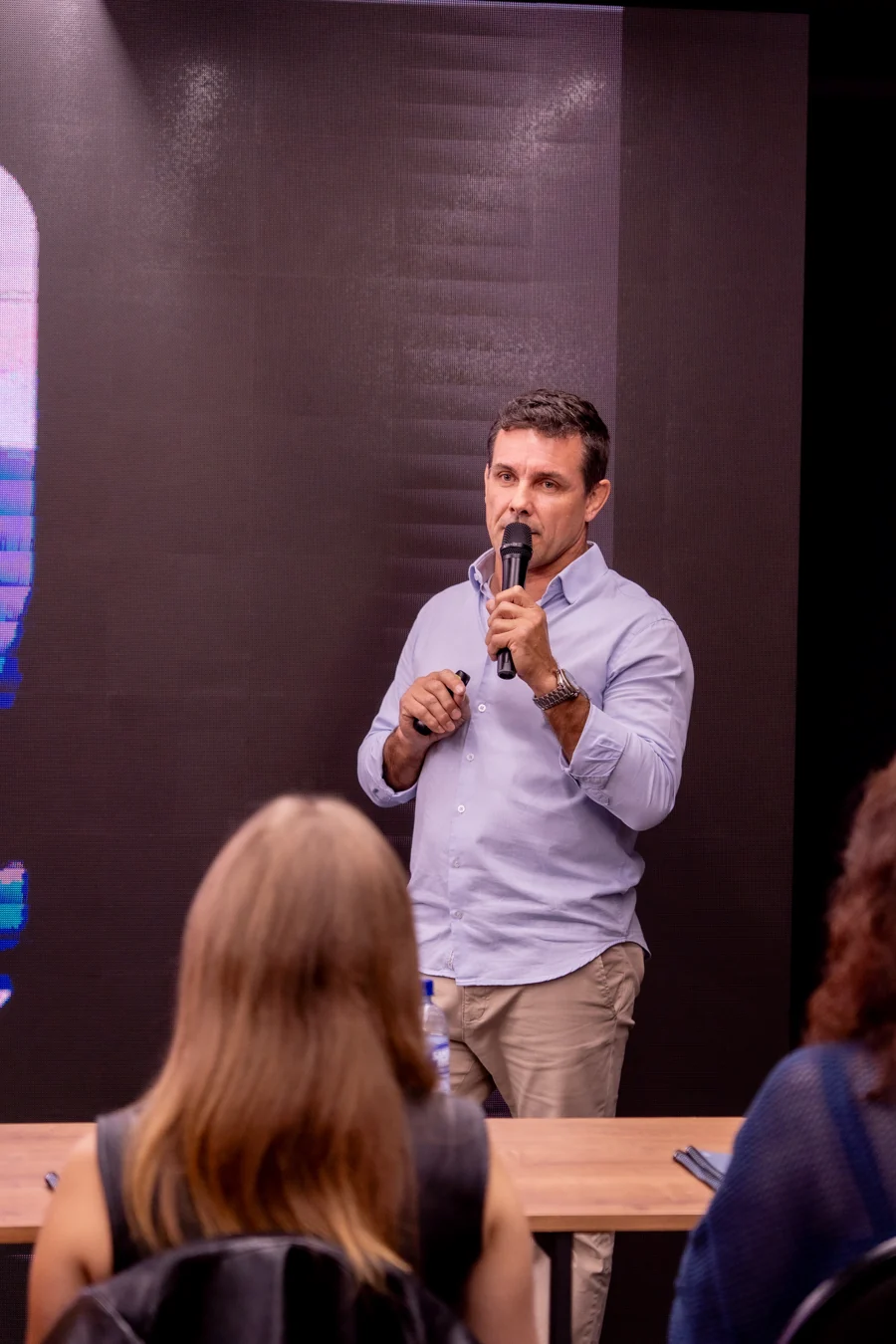 Rodrigo Fontana conduzindo a oficina presencial com microfone e participantes à frente